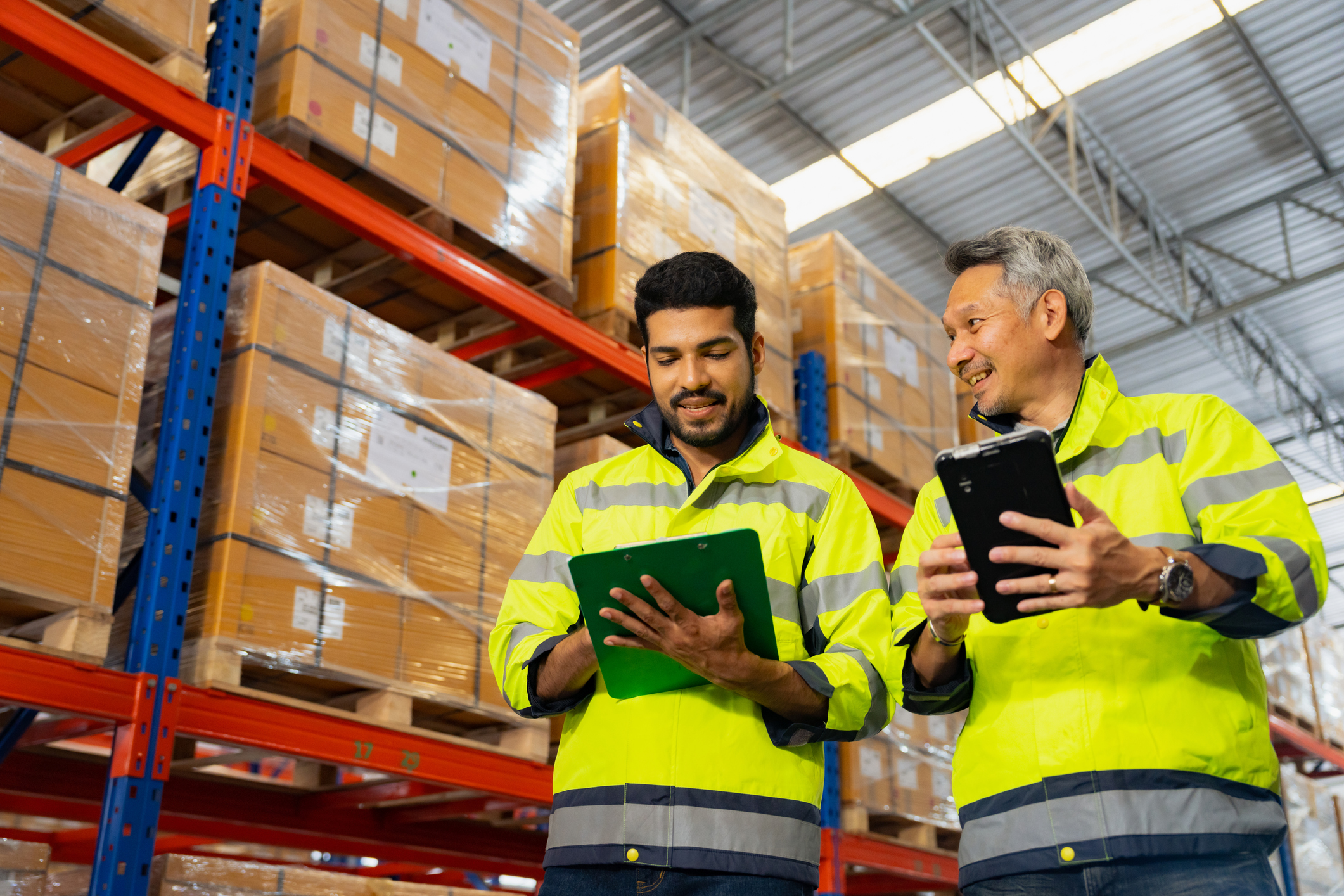 Asian two man supervisor walking in warehouse at a distribution warehouse. Warehouse employees using the company’s ERP software from their tablet computers.