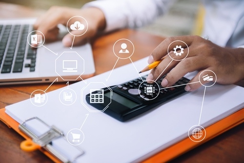 Person using a calculator and laptop with ERP software module icons, illustrating the comparison between Epicor and QuickBooks for manufacturing and distribution businesses.