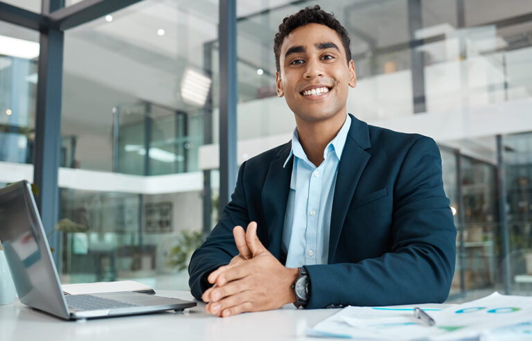 Professional smiling at a desk in a modern office.